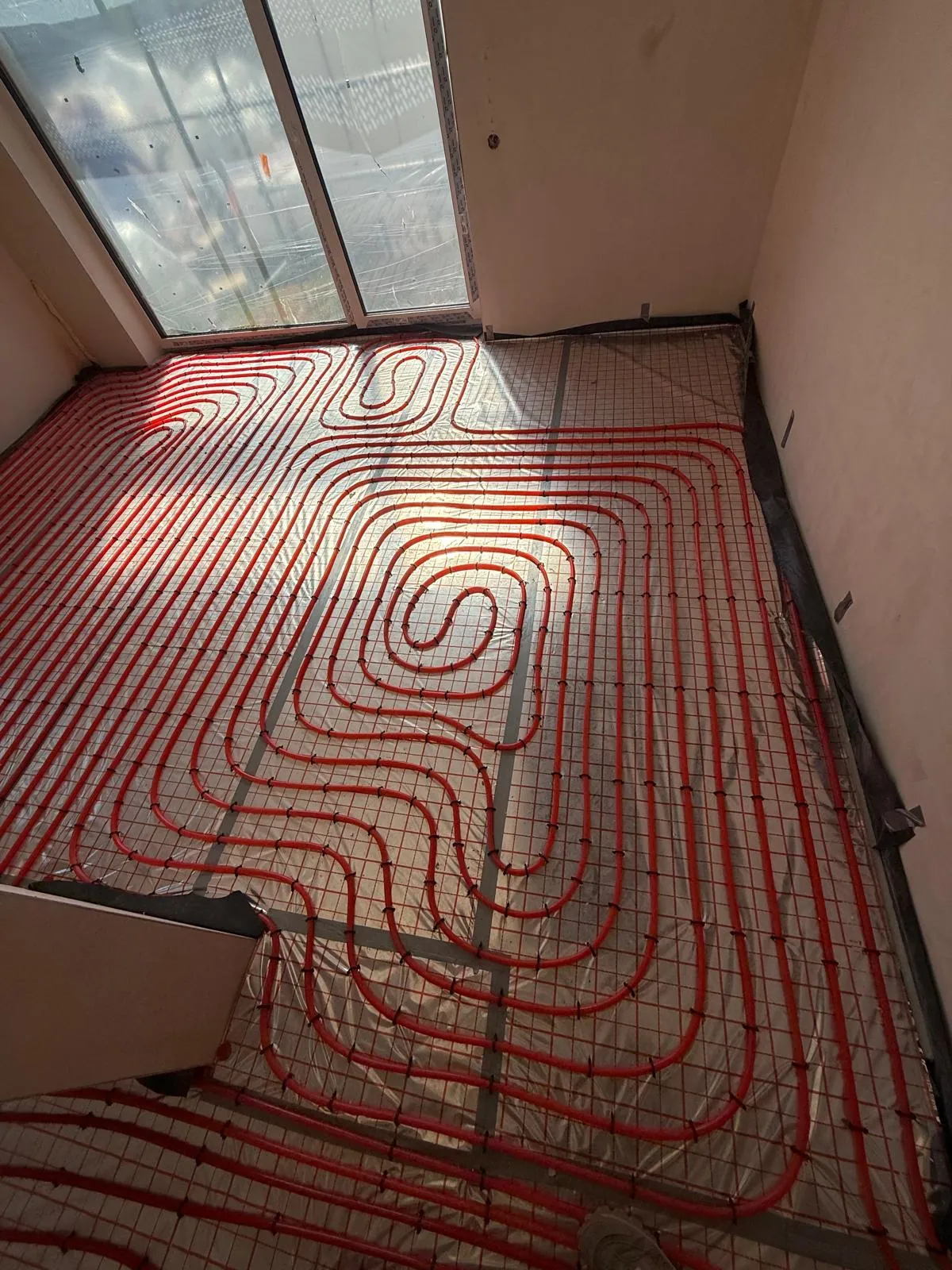 Ogrzewanie podłogowe z czerwonych rur ułożonych spiralnie w pokoju z dużym oknem